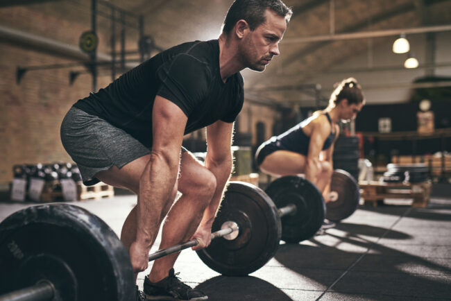Sporty,Man,And,Woman,Are,About,To,Lift,Barbells,In